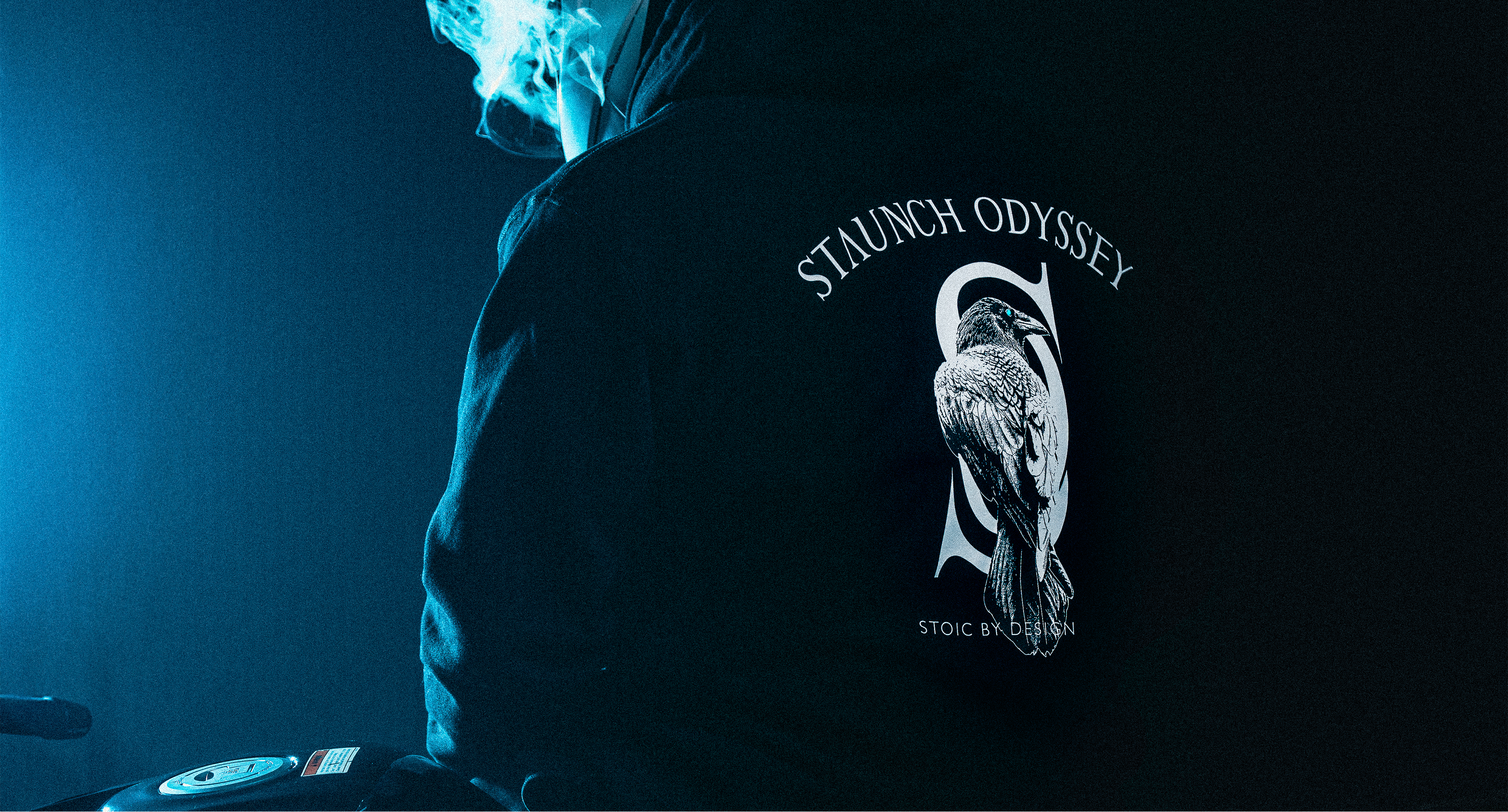 Person wearing a hoodie with 'Staunch Odyssey' logo on the back, blue lighting.